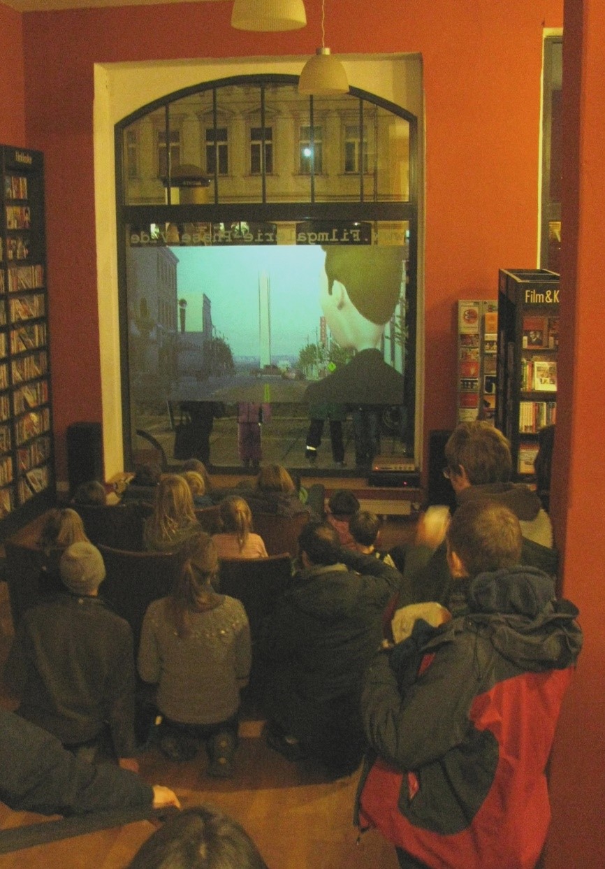 Mehrere Personen schauen einen Film, der auf eine Schaufensterscheibe projiziert wird.