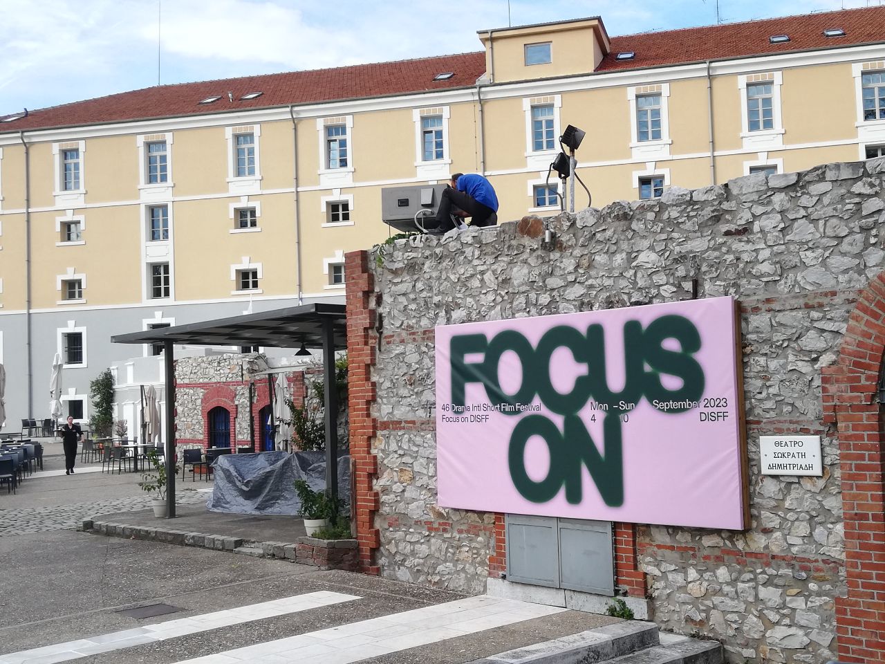 A house wall with a pink banner, on it is written large Focus On and small the name of the festival and the festival dates.